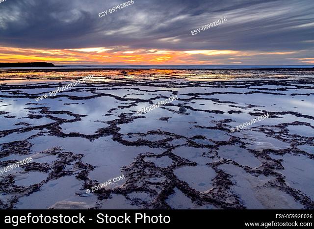 A beautiful sunset over the ocean with rocky beach and tidal pools in the foreground