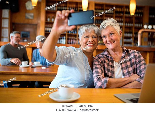 Senior friends taking selfie with mobile phone in restaurant