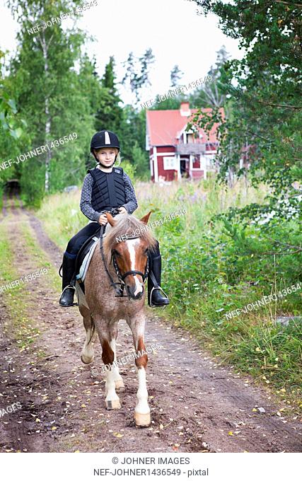 Girl horseback riding on rural road