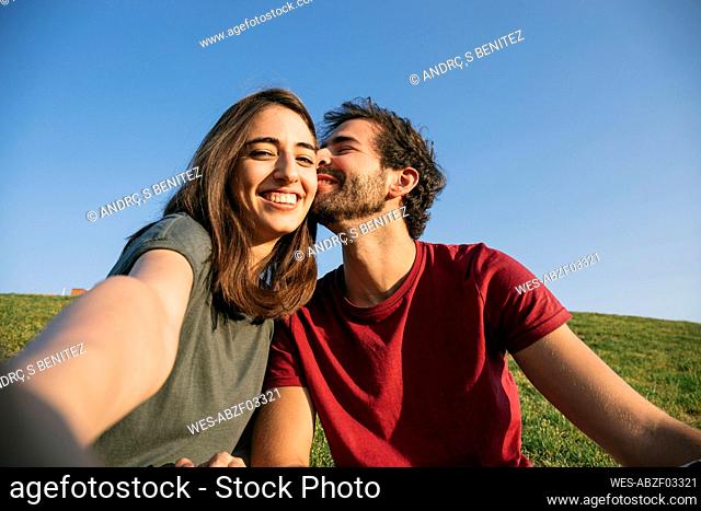 Woman taking selfie with man while sitting on grass