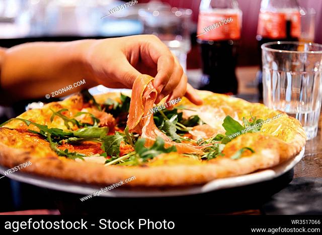 Hand of woman take ham pieces out from pizza plate in restaurant