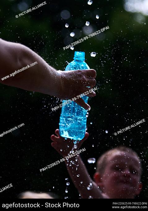 25 June 2022, Berlin: A mother fills water from the fountain for her son. The heat is sweltering in Berlin this weekend. Photo: Annette Riedl/dpa