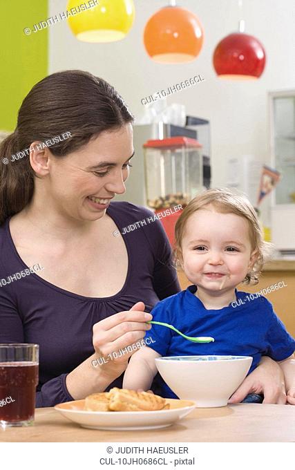 Mother feeding young girl, happy