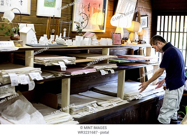 Japanese man in a traditional workshop with a display of handcrafted washi papers and small objects