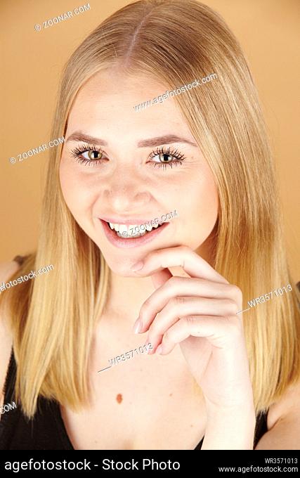Attraktive junge blonde Frau hält ihre Hand ans Gesicht isoliert vor braunem Hintergrund