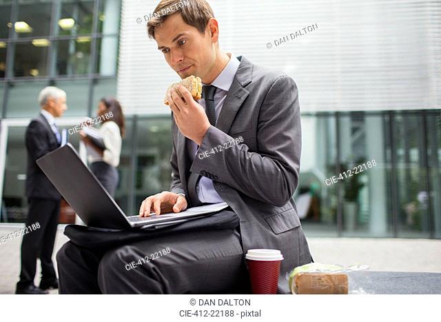 Businessman eating lunch while working outside office building