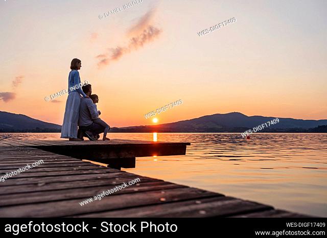 Family with daughter looking at sunset view from jetty, Mondsee, Austria