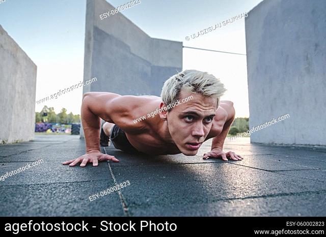 Young athletic man doing push ups on parkour area. Training alone outdoors