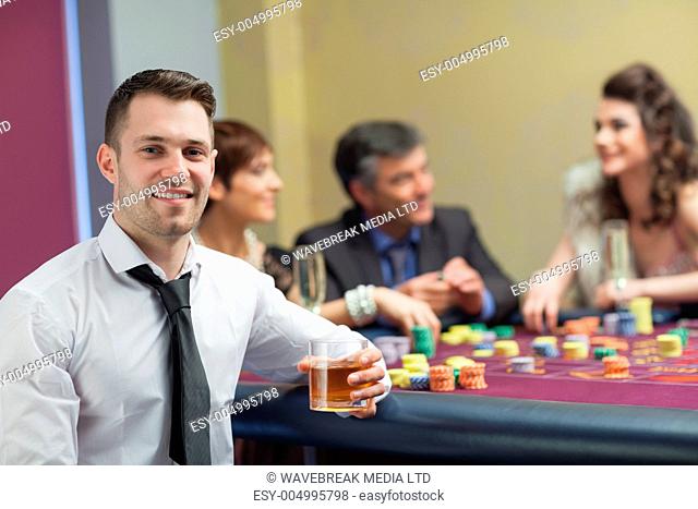 Young man with whiskey looking up and smiling from roulette table