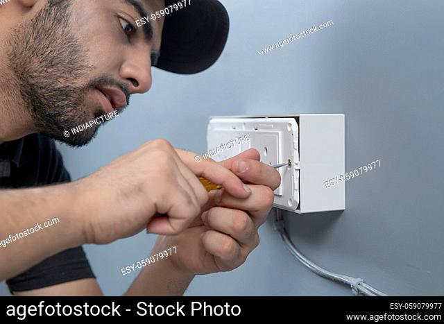AN ELECTRICIAN USING SCREWDRIVER TO OPEN SWITCHBOARD