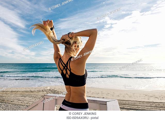 Young woman on lifeguard platform, putting hair up, rear view