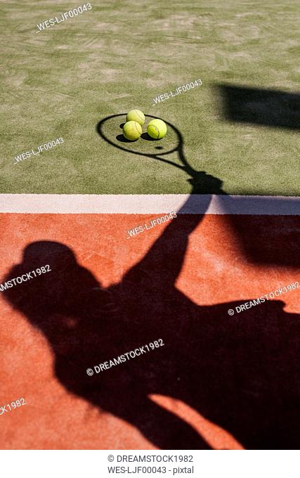 Shadow of a tennis player with balls and racket on court