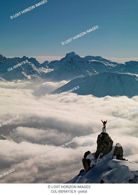 Climber celebrating on peak emerging from fog, Bettmeralp, Valais, Switzerland