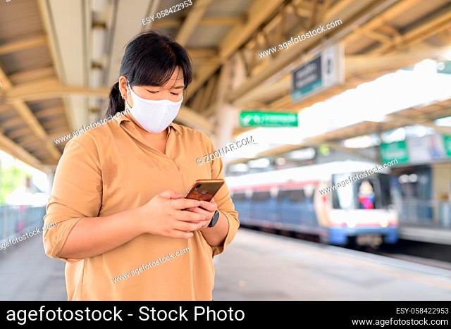 Portrait of overweight Asian woman with mask for protection from corona virus outbreak at the sky train station
