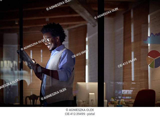 Smiling businesswoman working late, using digital tablet in dark office at night
