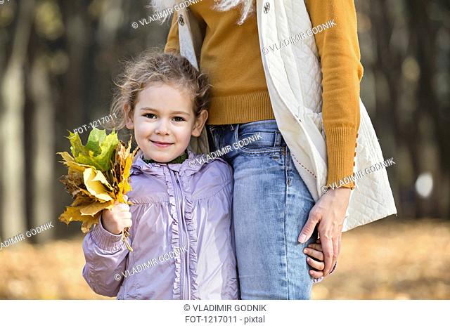 A young girl holding a bouquet of autumn leaves and holding onto her Mom