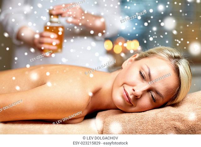 people, beauty, spa, winter and relaxation concept - close up of beautiful young woman lying with closed eyes on massage table and therapist holding oil bottle...