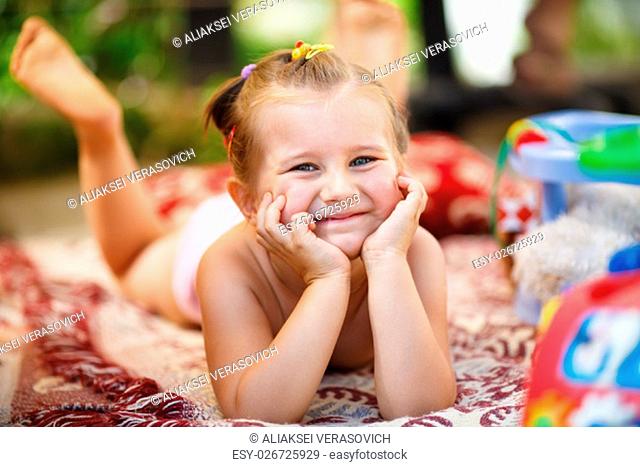 Happy smiling baby girl lying on a blanket outdoors. Little girl resting his head on his hands and looking into the camera. Shallow depth of field