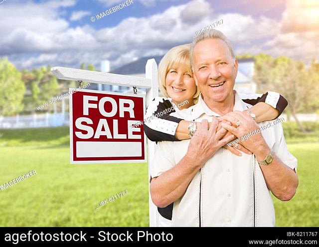 Happy senior couple front of for sale real estate sign and house