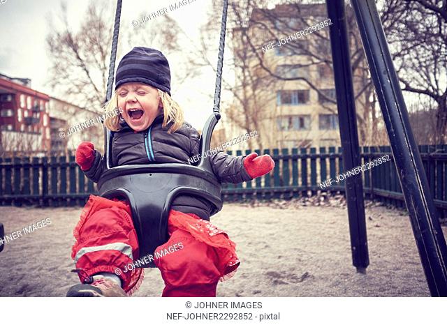 Cheerful girl swinging in playground