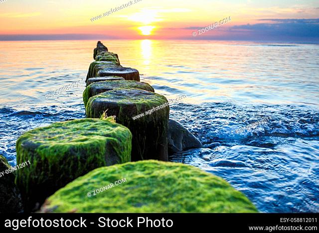 Wooden spur dykes in coastal sunset. Old groynes and wavy sea water, Baltic Sea, Island of Hiddensee, Germany
