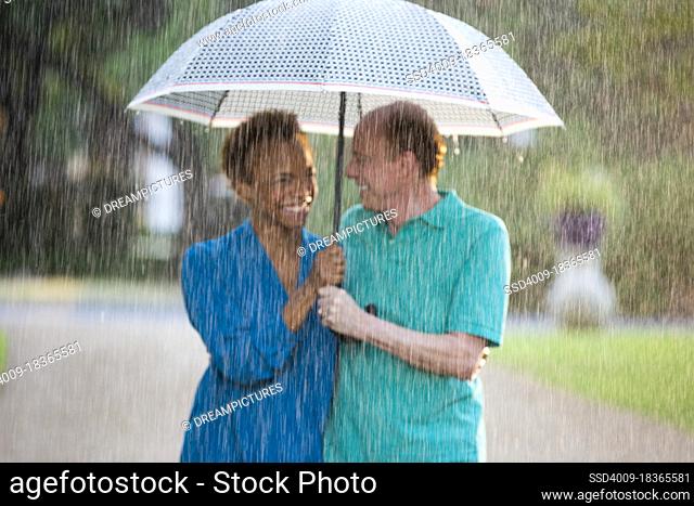 Older couple walking through park with umbrella in the rain, out of focus