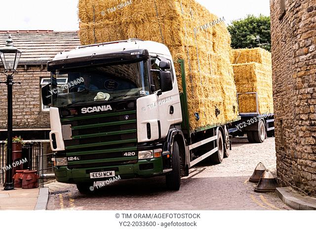 A Scania articulated lorry carrying straw bales driving through the narrow streets of Hawes in Wensleydale , North Yorkshire, England, Britain, Uk