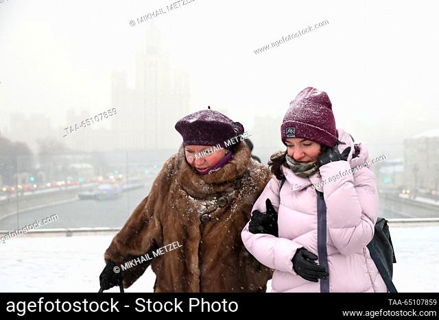 RUSSIA, MOSCOW - NOVEMBER 23, 2023: People walk in Zaryadye Park during a snowfall with a high-rise residential building on Kotelnicheskaya Embankment in the...