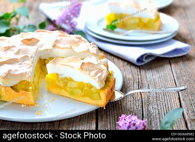 Leckerer Rhabarberkuchen mit Baiserhaube auf einem Holztisch mit frühlingshafter Fliederdeko - Delicious rhubarb cake with springlike lilac decoration