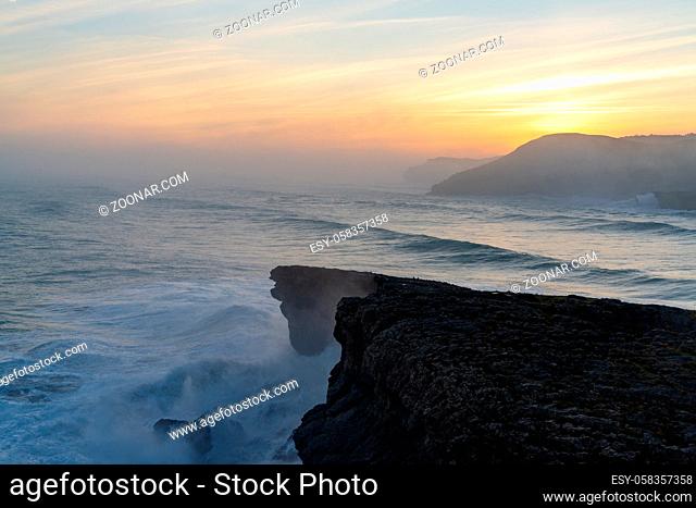 A view of huge storm surge ocean waves crashing onto shore and cliffs at sunrise