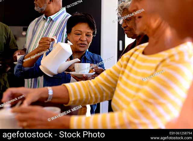 Biracial senior woman serving coffee to multiracial friends while sitting in nursing home