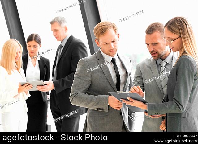 Three smart employees discussing documents using tablet pc at meeting