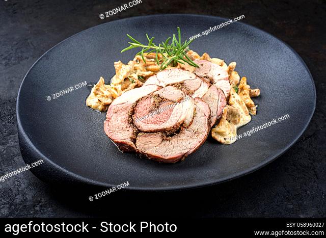 Traditional French barbecue lamb roast sliced with chanterelles in cream sauce offered as close-up on a design cast-iron plate