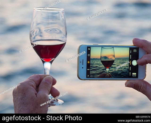 Tourist taking pictures of wine glass and sunset with his smartphone, Zadar, Dalmatia, Croatia, Europe