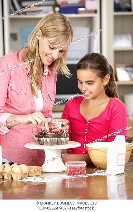 Mother And Daughter Decorating Homemade Cupcakes In Kitchen