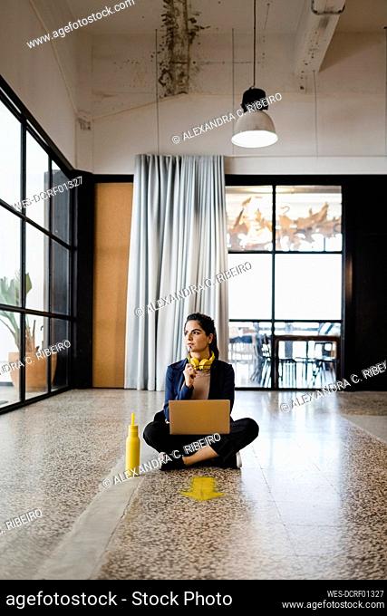 Contemplative young businesswoman sitting on ground in office