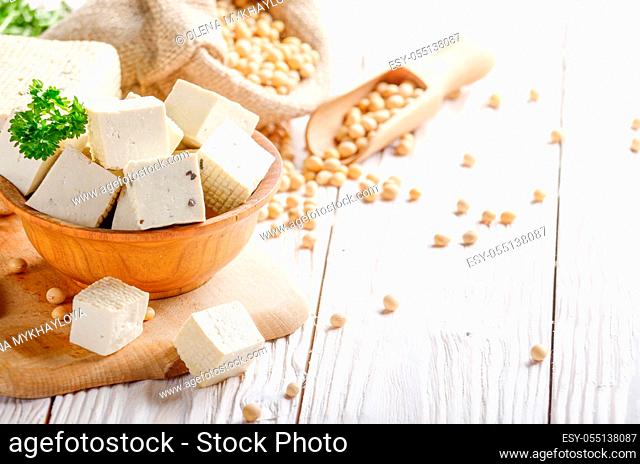 Soy Bean curd tofu in wooden bowl and in hemp sack on white wooden kitchen table. Non-dairy alternative substitute for cheese. Place for text