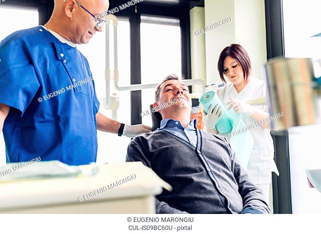 Male patient in dentist chair, dentist standing beside him