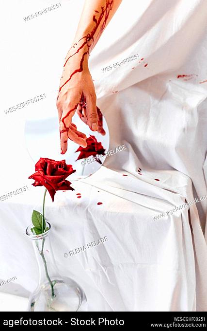 Woman with bloody hand touching red rose in flower vase
