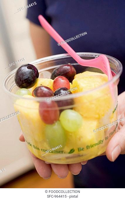 Woman holding plastic tub of fruit salad with fork