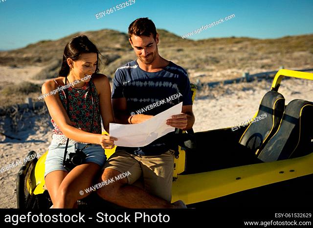Happy caucasian couple sitting on beach buggy by the sea reading roadmap