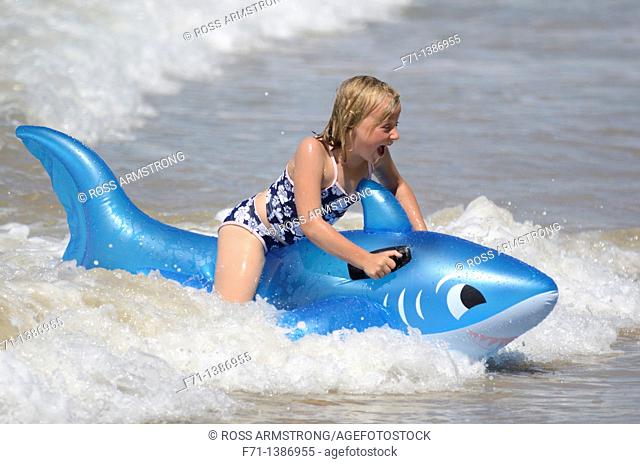 Six year old girl at the beach playing in the surf on inflatable shark Mimiwhangata Northland, New Zealand