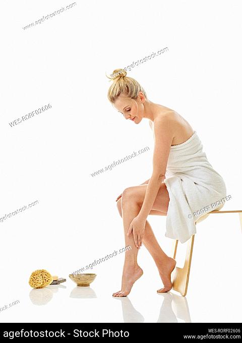 Young woman wrapped in towel while sitting on chair against white background