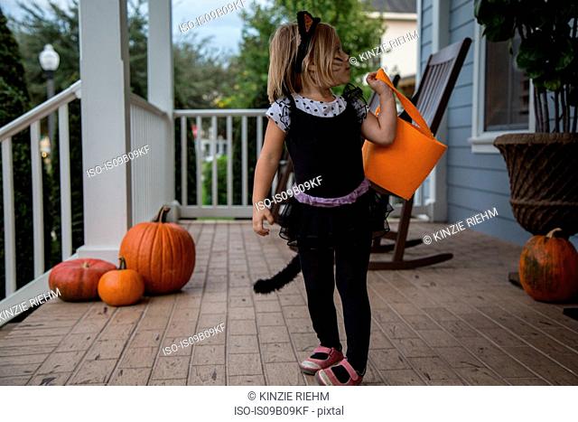 Girl trick or treating in cat costume looking over her shoulder on porch