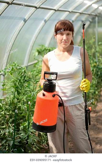 Female gardener with knapsack garden spray in hothouse