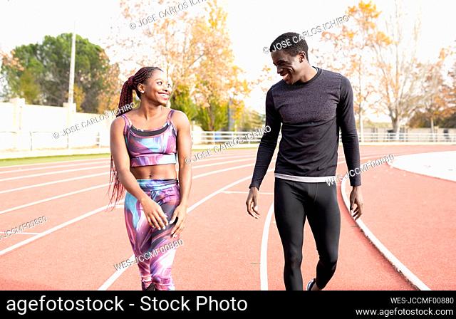 Happy male and female sportsperson walking on running track during sunny day