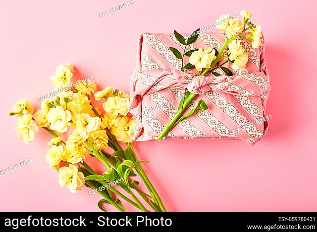 Bouquet of yellow matthiola with gift wrap in traditional japanese furoshiki style. Design concept of holiday greeting on pink table