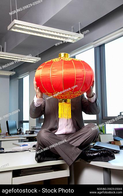 Businessman holding Chinese lantern in front of face