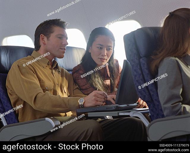 Young woman and man using laptop on airplane