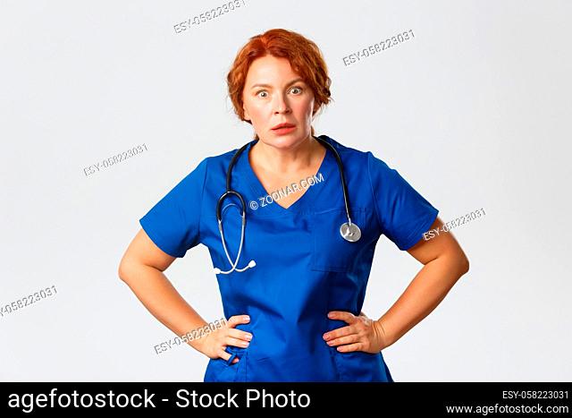 Medicine, healthcare and coronavirus concept. Shocked and speechless redhead female nurse, doctor in scrubs hear something inbelievable